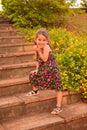 Little Spanish kid with a cute face posing for a picture in a park while sitting on the stairs