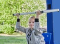 A little sporty girl in a sports uniform is engaged in the exercise machines on the playground for fitness on the street