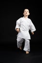 Little strong boy in kimono goes forward, practices karate, black background