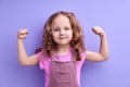 Little strong sporty fitness kid girl showing biceps muscles on hand isolated on purple