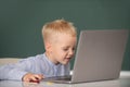Little student boy using laptop computer in school class. Funny blonde pupil on blackboard. Royalty Free Stock Photo