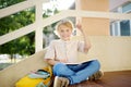 Little student doing homework on break on stair of elementary school building. Cute boy having idea and showing forefinger up. Royalty Free Stock Photo
