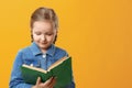 Little student girl in denim shirt on yellow background. The child is reading a book. The concept of education and school Royalty Free Stock Photo