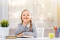 Little student girl sitting at the table and reading a book. The child shows a sign shh. The concept of education and school.