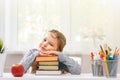 Little student girl sitting at the table. Tired schoolgirl with a pile of books. Education. Back to school. In the background is