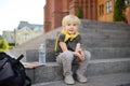 Little student sitting on staircase near the school building. Back to school