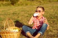 Little stylish boy in sunglasses is drinking yogurt on the meadow