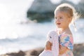 Little surprised girl stands on the beach hugging a toy hare Royalty Free Stock Photo