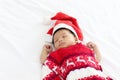 A little sweet adorable infant newborn baby with Christmas sweater and Santa hat sleeping happily on white warm bed near teddy Royalty Free Stock Photo