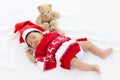 A little sweet adorable newborn infant baby with Christmas sweater and Santa hat sleeping happily on white warm bed near teddy Royalty Free Stock Photo