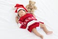 A little sweet adorable newborn infant baby with Christmas sweater and Santa hat sleeping happily on white warm bed near teddy Royalty Free Stock Photo