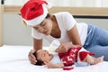 A little sweet adorable newborn infant baby girl lying on white bed with mom who wearing red Christmas Santa hat and holding milk Royalty Free Stock Photo