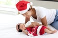 A little sweet adorable newborn infant baby girl lying on white bed with mom who wearing red Christmas Santa hat and holding milk Royalty Free Stock Photo