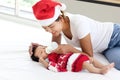 A little sweet adorable newborn infant baby girl lying on white bed with mom who wearing red Christmas Santa hat and holding milk Royalty Free Stock Photo