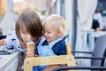 Little sweet toddler boy, eating ice cream from a cone, sitting in high chair in beach restaurant, his older brothers sneaking and Royalty Free Stock Photo