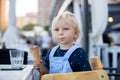 Little sweet toddler boy, eating ice cream from a cone, sitting in high chair in beach restaurant Royalty Free Stock Photo