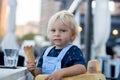 Little sweet toddler boy, eating ice cream from a cone, sitting in high chair in beach restaurant Royalty Free Stock Photo