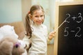 Little teacher. Beautiful young girl is teaching toys at home on blackboard. Royalty Free Stock Photo