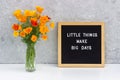 Little things make big days. Motivational quote on letter board and bouquet orange flowers on white table against grey