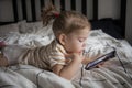 Little toddle girl playing with smartphone laying on the bed at home. Caucasian toddler girl.