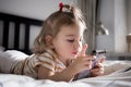 Little toddle girl playing with smartphone laying on the bed at home. Caucasian toddler girl.