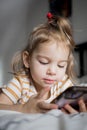 Little toddle girl playing with smartphone laying on the bed at home. Caucasian toddler girl.