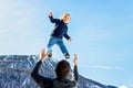 Little toddler boy, flying in the sky, dad throwing him high in the air. Family, enjoying winter view of snowy mountains and Royalty Free Stock Photo