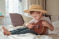 Little toddler boy in hat playing ukulele guitar at home, rustic style. Lifestyle concept Royalty Free Stock Photo