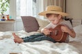 Little toddler boy in hat playing ukulele guitar at home, rustic style. Lifestyle concept Royalty Free Stock Photo