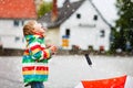 Little toddler boy playing on rainy day. Happy positive child having fun with catching rain drops. Kid with rain clothes