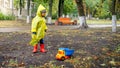 Little toddler boy in raincoat playing with toy truck at park on cold rainy day Royalty Free Stock Photo