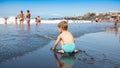 Little toddler boy sitting on the beach and playing with ocean waves Royalty Free Stock Photo