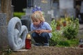 Little toddler boy, sitting on a grave in cemetery, sad and lonely, springtime