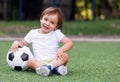 Little toddler boy sitting with legs crossed on football field in summer day with soccer ball. Happy active child Royalty Free Stock Photo