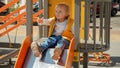 Little toddler boy sitting on top of the slide on playground and asking mother to hold his hand