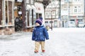 Little toddler boy walking through the snowy city during snowfall. Cute happy child in winter clothes having fun Royalty Free Stock Photo