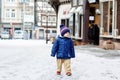 Little toddler boy walking through the snowy city during snowfall. Cute happy child in winter clothes having fun Royalty Free Stock Photo