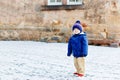 Little toddler boy walking through the snowy city during snowfall. Cute happy child in winter clothes having fun Royalty Free Stock Photo