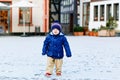 Little toddler boy walking through the snowy city during snowfall. Cute happy child in winter clothes having fun Royalty Free Stock Photo