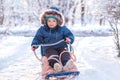 Little toddler child in blue winter jacket and hood sitting with surprised face in sledge on bright snowy day. Happy childhood Royalty Free Stock Photo