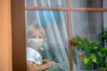 Little toddler child, boy, sitting sad on a window shield, looking outside at sunset, wearing protective medical mask Royalty Free Stock Photo