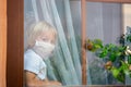 Little toddler child, boy, sitting sad on a window shield, looking outside at sunset, wearing protective medical mask Royalty Free Stock Photo