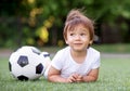 Little toddler child laying on belly on football field near soccer ball and dreaming. Wind is waving hair of kid. Future sportsman