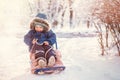 Happy toddler kid sits on sled under snowfall and laughs hiding from snow. Toned image. Place for copy text Royalty Free Stock Photo