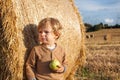 Little toddler eating apple with a big hay bale on field Royalty Free Stock Photo