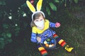 Little toddler girl with bunny ears having fun with traditional Easter eggs hunt on spring day, outdoors. Happy child