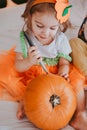 Little toddler girl drawing on a pumpkin making lantern jack on Halloween holiday. Little girl in a carnival costume Royalty Free Stock Photo