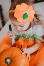 Little toddler girl drawing on a pumpkin making lantern jack on Halloween holiday. Little girl in a carnival costume