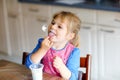 Little toddler girl eating yogurt for breakfast. Cute healthy baby sitting in the kitchen or at nursery and having meal. Royalty Free Stock Photo