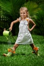 A little toddler girl girl is watering flowers in her green rubber boots from a watering can. Royalty Free Stock Photo